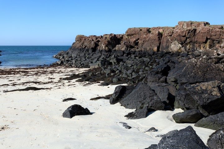 Black rocks on the sandy beach of Port Na Ba, Isle of Mull, Inner Hebrides of Scotland